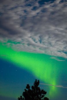 Intense Aurora borealis showing between clouds during moon lit night.