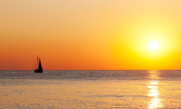 Golden sunset on a sea with silhouette of a yacht.