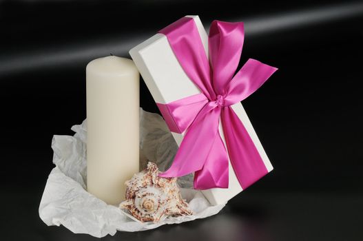 Gift box with ribbon, decorated with candles and sea shells. On a dark background.