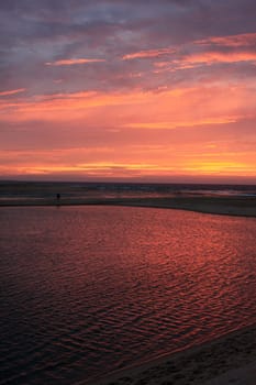 view of a lonely figure on the shore of a beach at sunset.