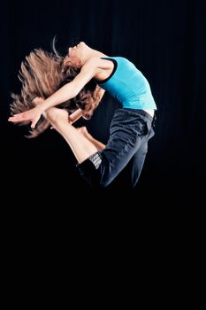 Young woman in tracksuit jumping on black background