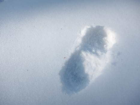 A single bootprint in the snow, outlined by shadows and sunlight.