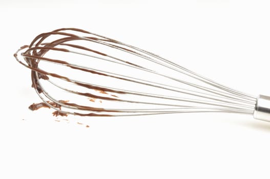 Whisk with chocolate cream on a white background