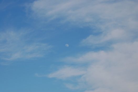 Daylight moon shining in a blue cloudy sky