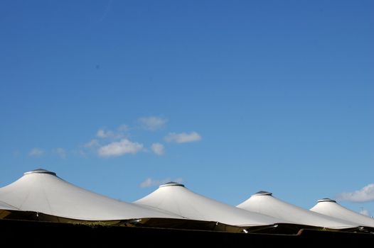 Line of white marquee rooftops against a pale blue sky with small fluffy white clouds.