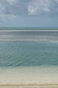Calm ocean view from beach to horizon with the reflection of a pale blue sky in the pale turquoise water