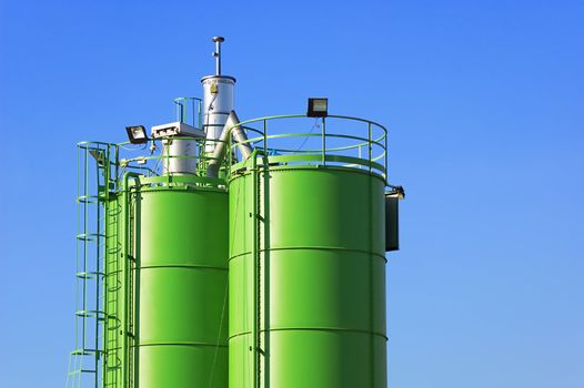 Two green silos agaist blue sky in a construction site