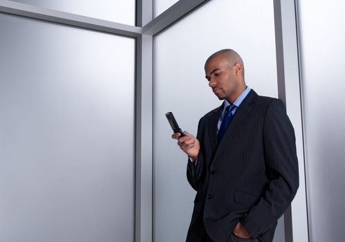 Businessman beside an office window, sending a message with his cell phone.