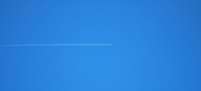 Passenger jet plane on clear, blue sky. Vapor traces parallel to the image edge. 