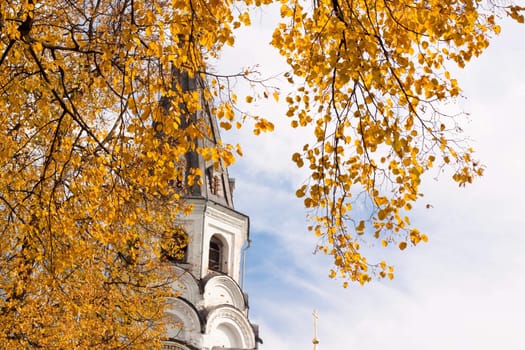 Yellow autumn leaves, white old church and sky
