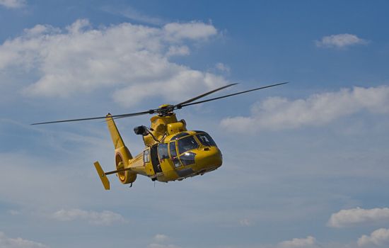 Flight of yellow helicopter in blue sky with clouds 