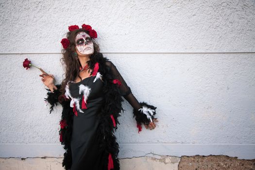 Woman in makeup for All Souls Day stands alongside a wall with red roses