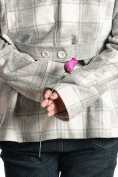 A young teenage girl is standing with a wooden rose behind her back.