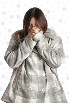 A cold teenage girl is breathing into her hands to warm them up while wearing a fall or winter jacket.