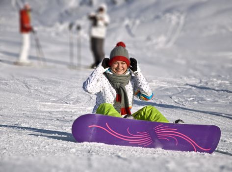 Beautiful woman snowboarder sitting on the ski slope. Adjusts his cap and smiling. Tilt Shift.
