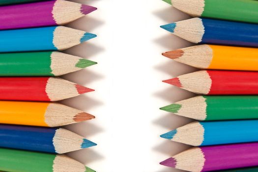 Close up capturing a selection of coloured artist pencils in arranged in a regular format over white.