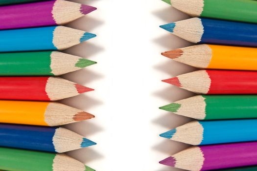 Close up capturing a selection of coloured artist pencils in arranged in a regular format over white.