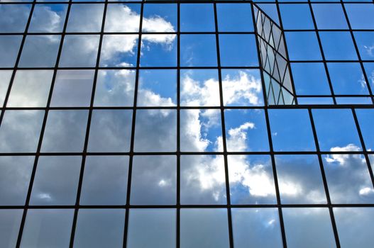 Modern glass office building with clouds and sky reflections.