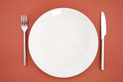 top view of white plate, fork and knife, restaurant tableware