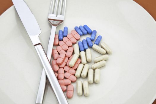 Vitamin pills and capsules on plate with knife and fork, a meal of pills