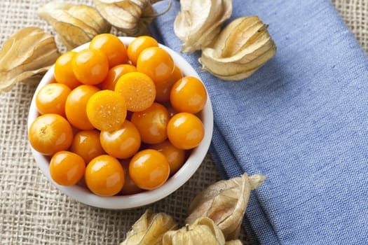 Physalis fruit with one cut in half in bowl on blue napkin and burlap.