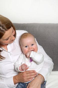 Smiling mother holding her baby. The baby sits on her leg and smiles toward the camera.
