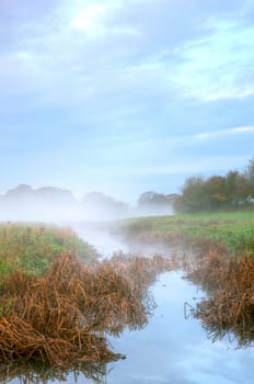 Beautiful foggy sunrise over calm stream in English countryside landscape