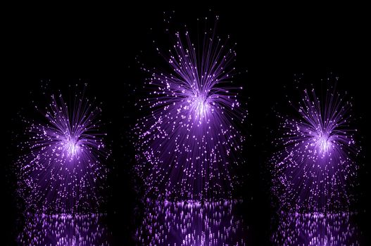 Low level angle capturing three violet groups of illuminated fibre optic light strands against a black background and reflecting into the foreground.