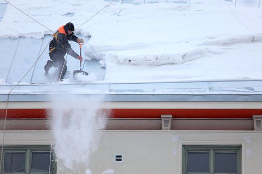 a man secured with ropes is de-icing and cleaning a snowy winter roof with a snow shovel