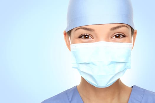 Doctor / nurse smiling behind surgeon mask. Closeup portrait of young asian caucasian woman model in blue medical scrub.