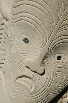 Carved maori face, close up, sandstone, with tattoo or moko imagery.