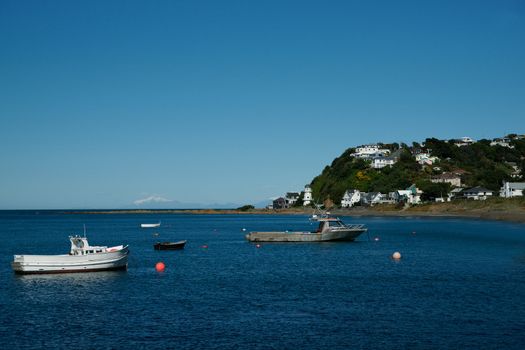 Island Bay, New Zealand, boats st idly on calm water with Southern Alps seen faintly on horizon.