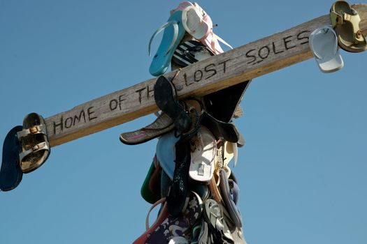 Old beach footwear attached symbolically to a wooden cross on beach.