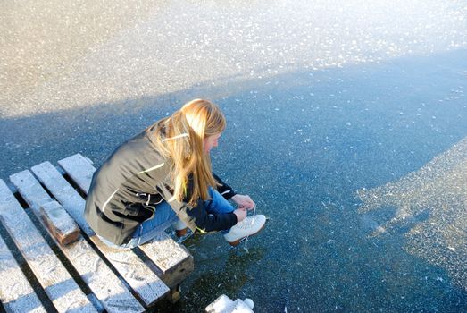 Young woman going to skate on frozen lake putting her ice skating shoes on.