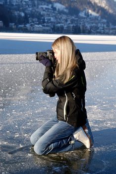 Woman kneeing on ice taking pictures on frozen lake
