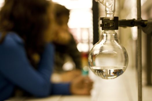 Focus on some chemistry equipment with students faded on the background.