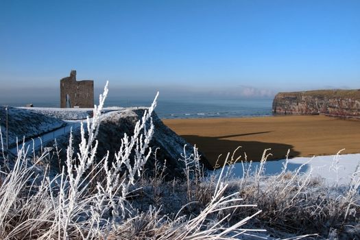 a seasonal snow covered view of atlantic ocean and ballybunion castle beach and cliffs on a frosty snow covered winters day