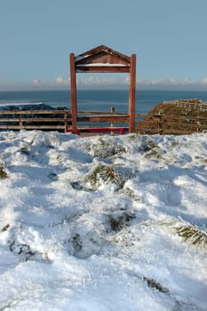 a seasonal snow frosty covered red bench framed with a sea view and blue cloudy sky background with copy space