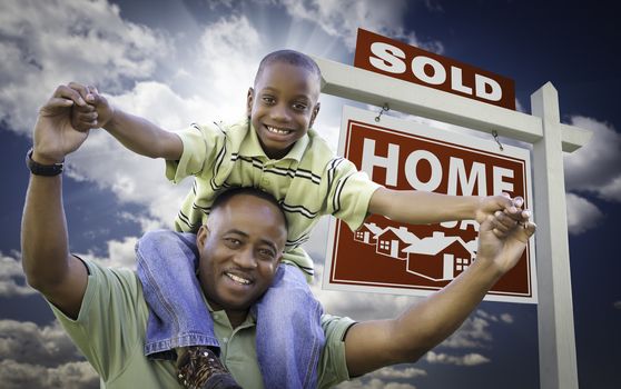 Happy African American Father with Son In Front of Sold Home For Sale Real Estate Sign and Sky.