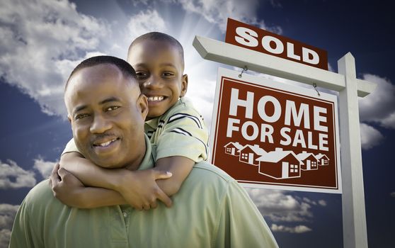 Happy African American Father with Son In Front of Sold Home For Sale Real Estate Sign and Sky.