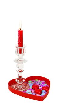 Red candle in glass candlestick on heart shaped tray with candies and sparkles