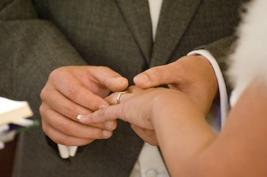 Close up detail of groom putting wedding ring on bride's finger during real ceremony