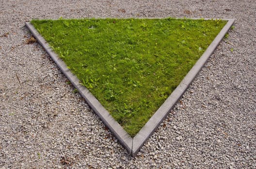 Green triangular island of grass surrounded by path in park.