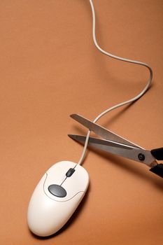 Scissors cutting cable of computer mouse on brown background