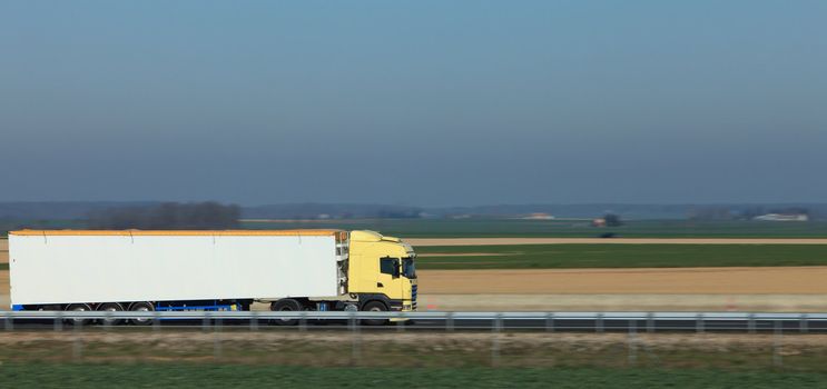 Panning image of a big white track on a highway in a plain area.