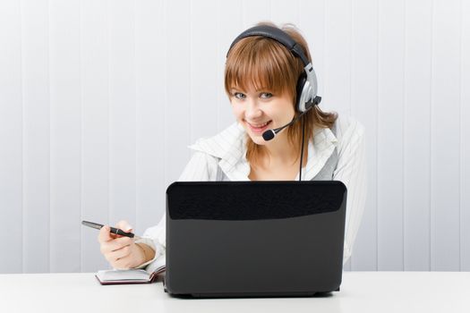 attractive smiling girl in headphones with a microphone works with a laptop and notebook
