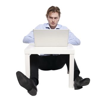 Young businessman, office worker or student with laptop, Studio photo of young man sitting at funny small table.