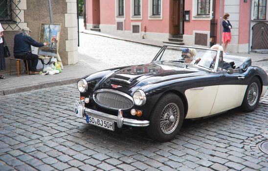RIGA, LATVIA - AUGUST 9: Senior couple driving retro car in a street of Riga old city center on the eve of the International Antique Car Rally Riga Retro on August 9, 2010, Riga.