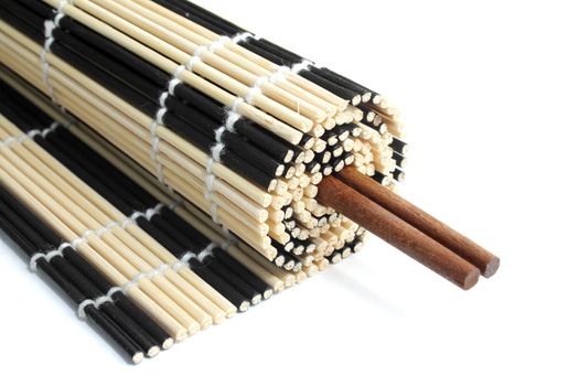 Rolled bamboo mat with a pair of chopsticks inside it on white background