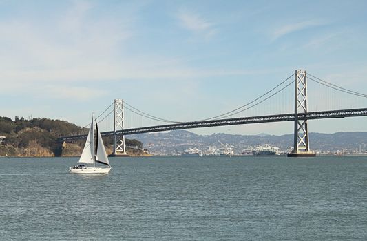 White sailboat on sunny day, with island and bridge as background